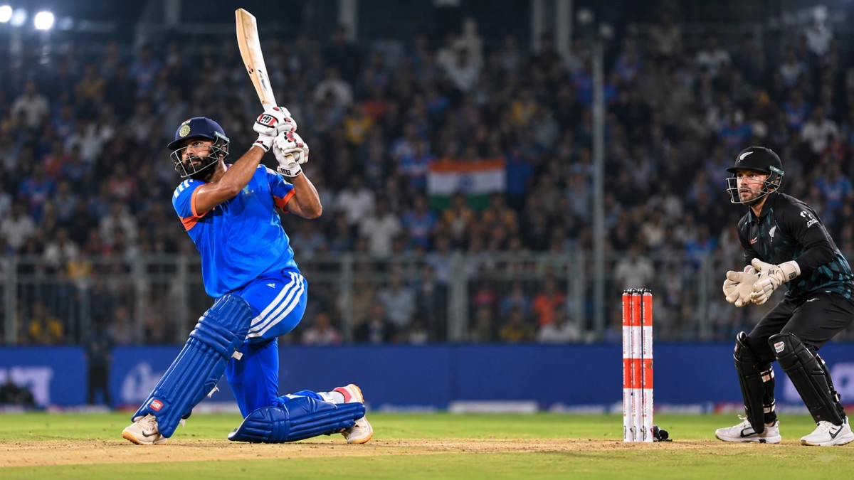 Illustration of an India batter in blue hitting a big shot as a New Zealand wicketkeeper watches at a floodlit ground