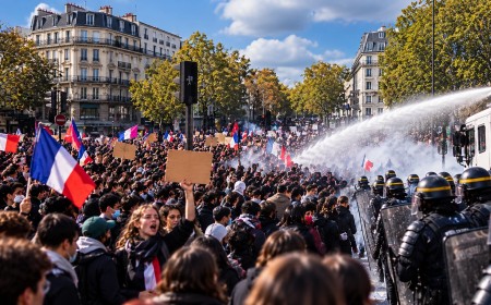 Illustration of young protesters with French flags facing riot police and a water cannon on a Paris street