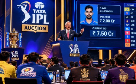 An auctioneer at a podium during a cricket player auction, with franchise tables in front.