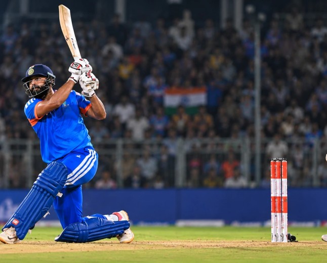 Illustration of an India batter in blue hitting a big shot as a New Zealand wicketkeeper watches at a floodlit ground
